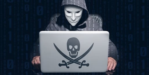 Guy with anonymous mask on using a laptop with a "skull & bones" sticker